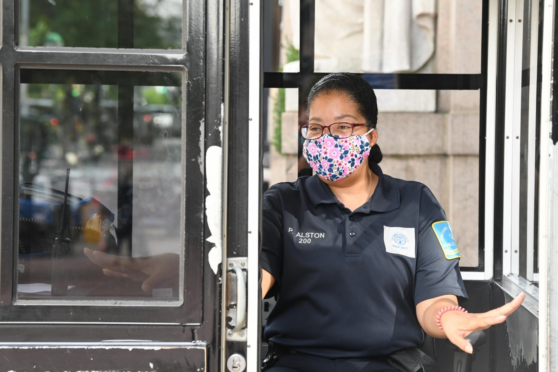 Public Safety officers often serve as ambassadors to campus, welcoming visitors as they enter and helping with directions or other assistance for anyone who asks. Female Public Safety Officer with glasses and a facemask on inside of a guard booth