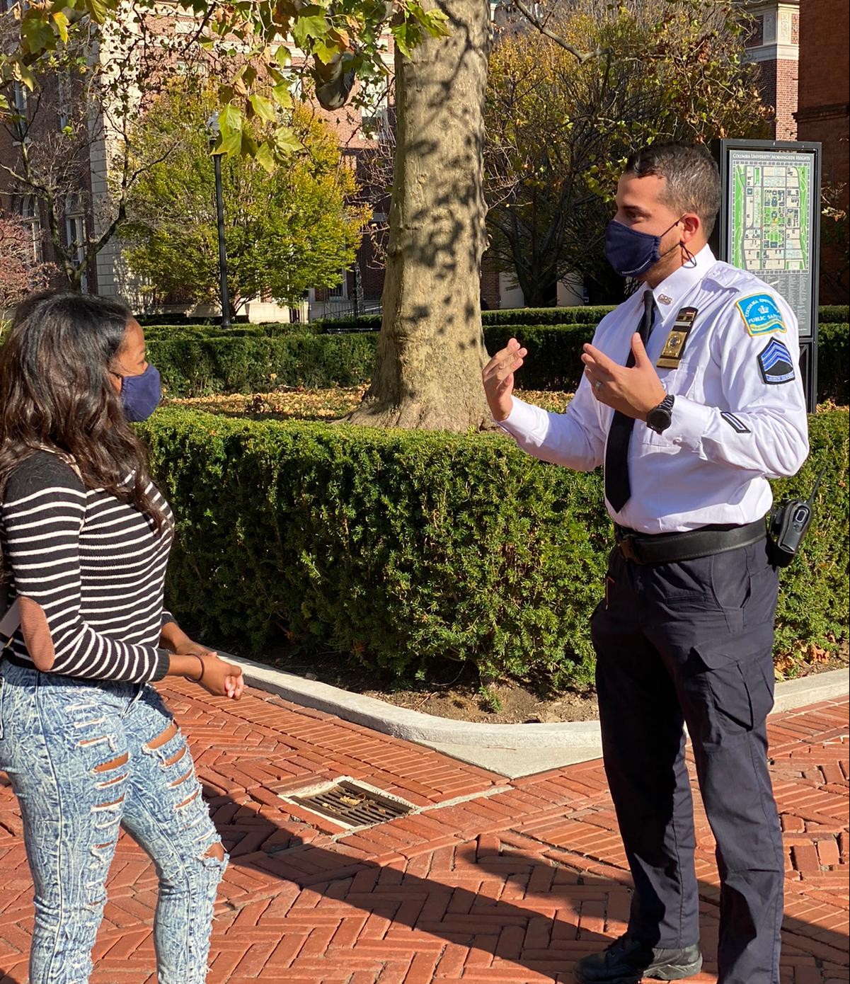 Public Safety personnel regularly patrol campuses, providing assistance to the community, greeting visitors, reporting malfunctioning lights, locks, call boxes, or other unsafe physical conditions. woman with a black and white striped shirt and a face mask on speaking to a CU public safety officer with a face mask in and in uniform on campus.