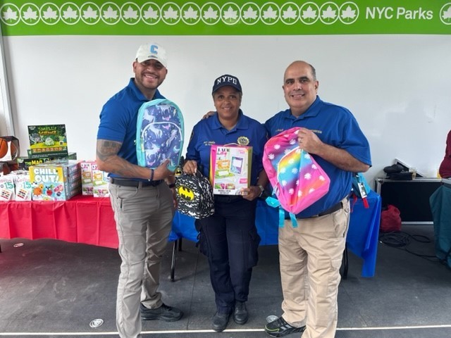 Two Public Safety officers and NYPD representative holding up school supplies