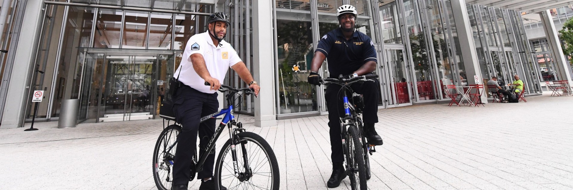 Two officers on bicycles posing in front of the Jerome L. Greene Science Center in Manhattanville