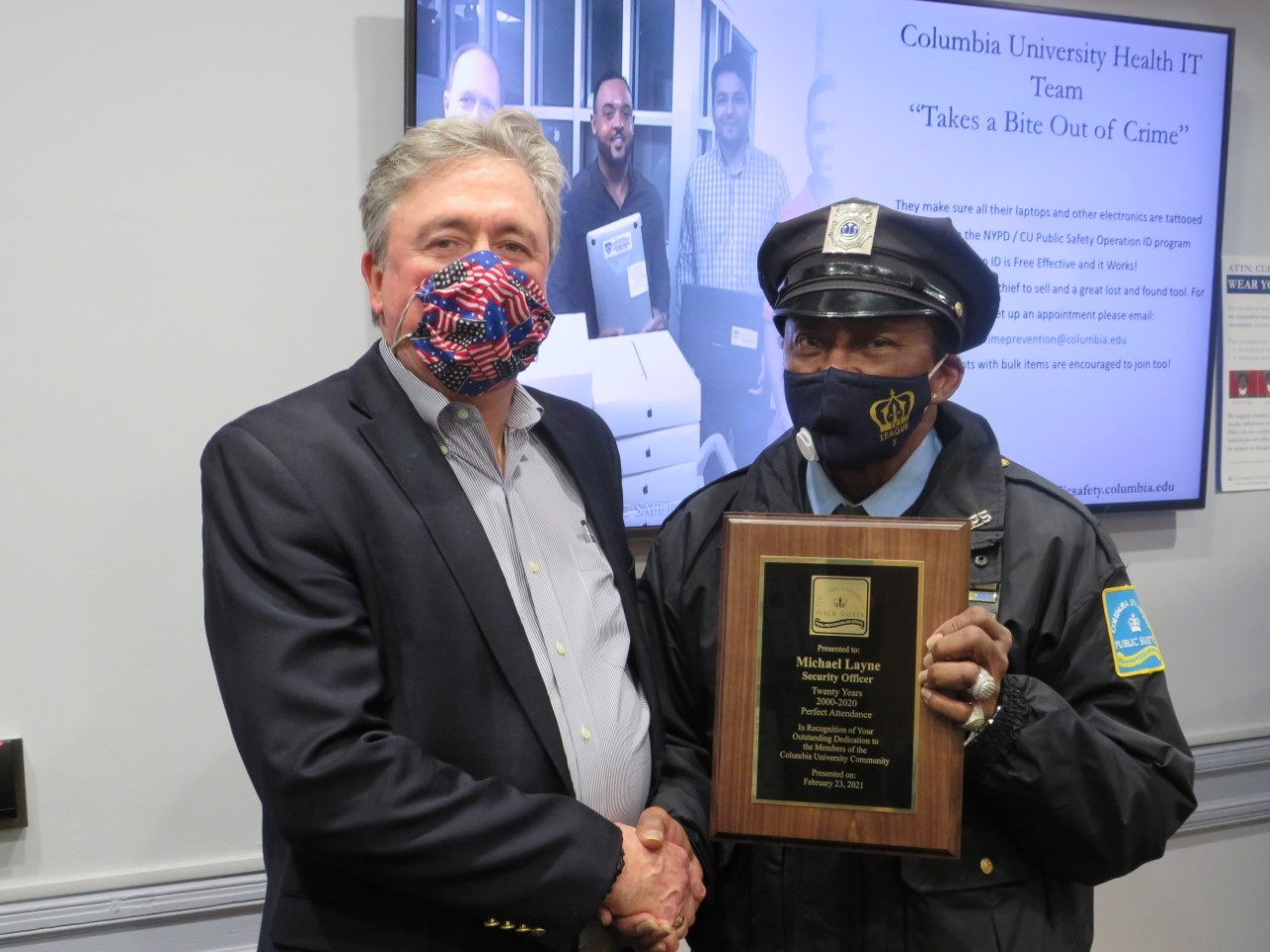 Vice President of Public Safety James McShane presents Public Safety Security Officer Michael Layne with plaque for 20 year of perfect attendance recognition. two men wearing masks and shaking hands