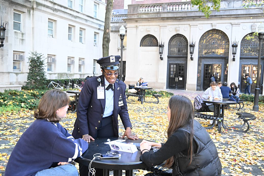 Public Safety personnel regularly patrol campuses, providing assistance to the community, greeting visitors, reporting malfunctioning lights, locks, call boxes, or other unsafe physical conditions. PSO female officer speaking to students in front of John Jay Hall