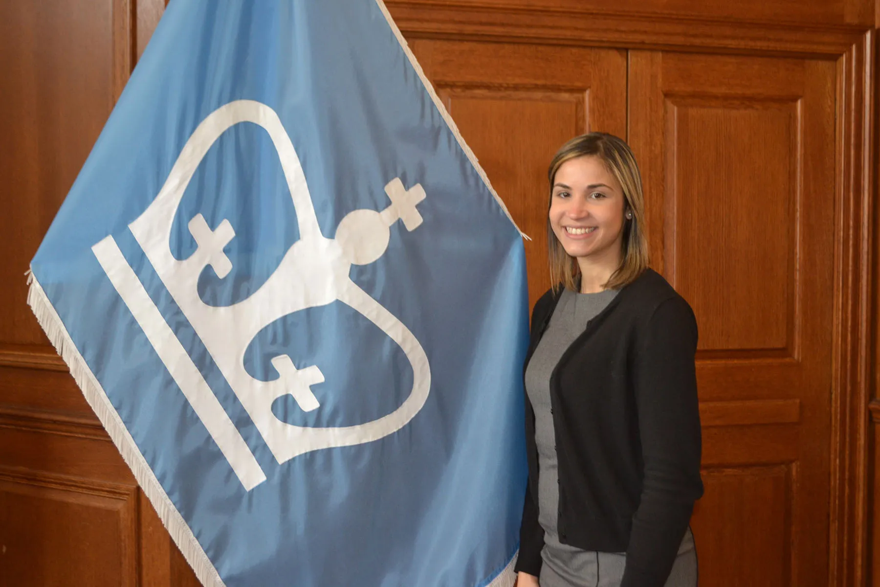 a woman standing in front of a brown wall and next to a Columbia University flag.