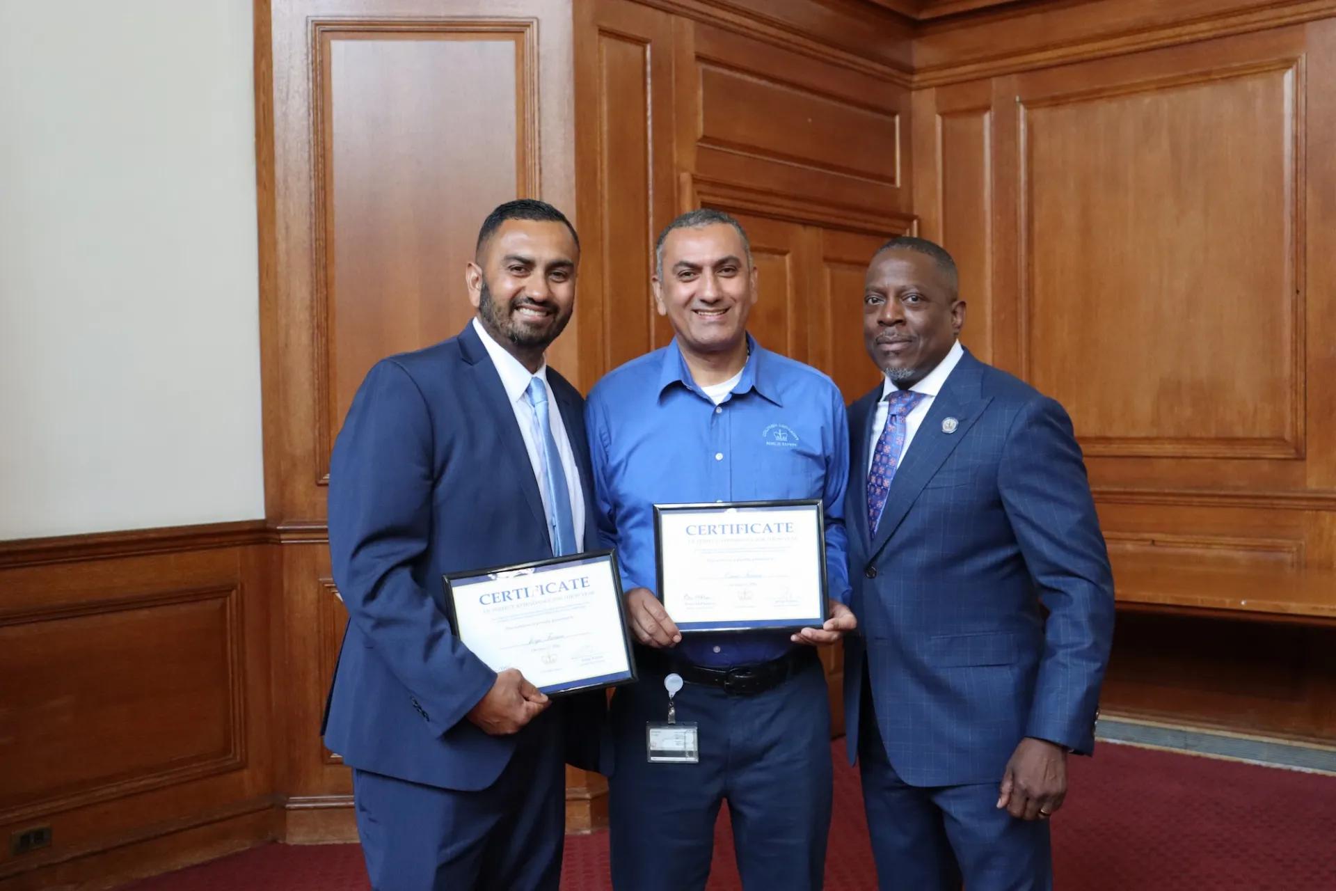 three men stand together two hold certificates